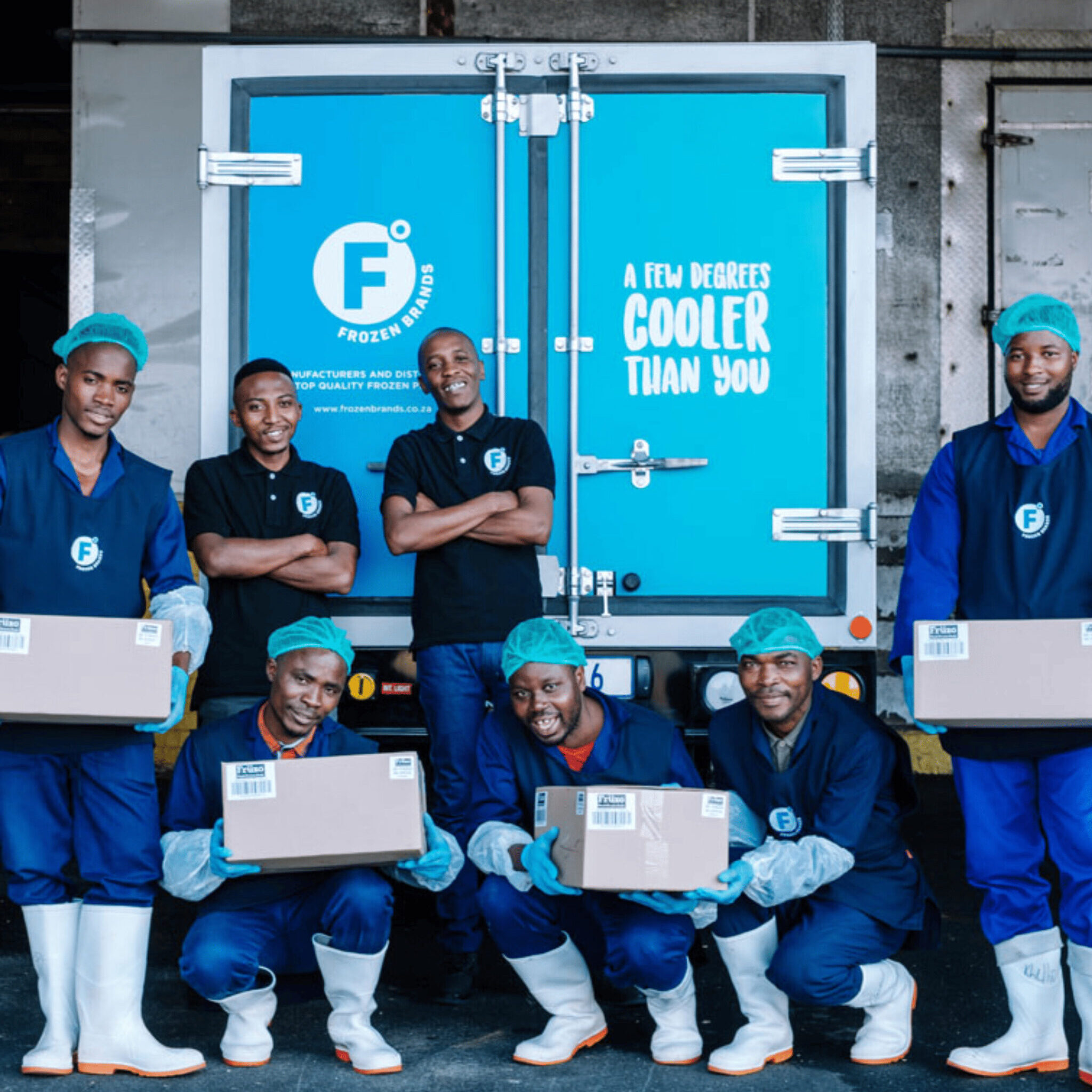 Group of smiling Frozen Brands factory workers standing outside in front of a Frozen Brands delivery truck.