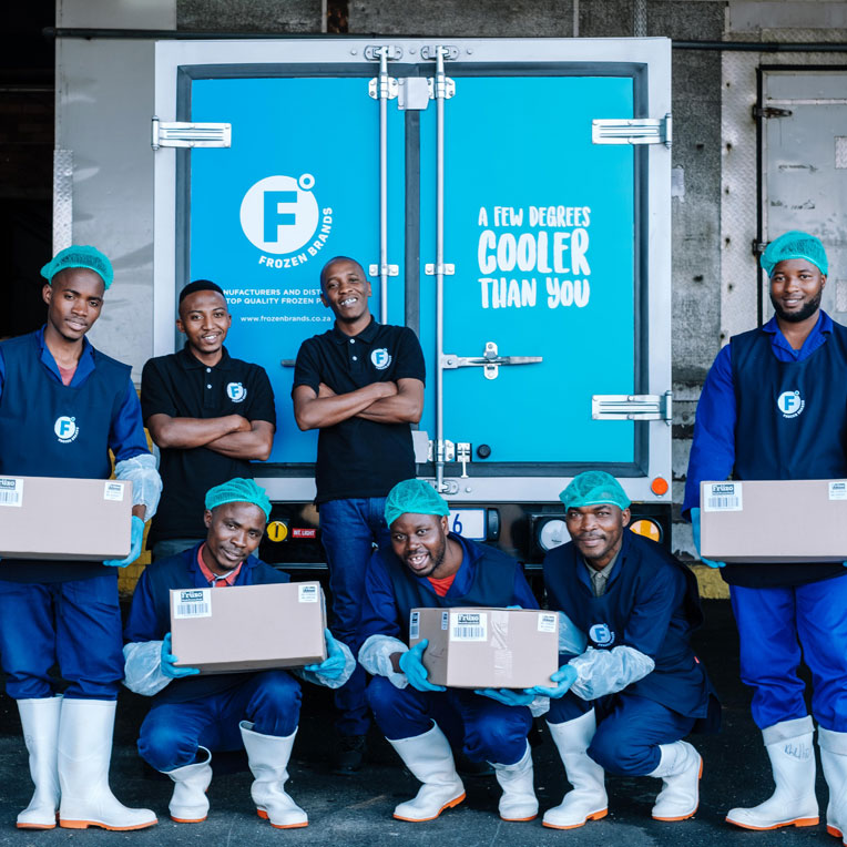 Group of smiling Frozen Brands factory workers standing outside in front of a Frozen Brands delivery truck.