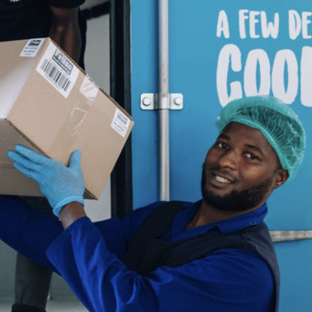 Food Services/Bulk supply – Our Offering – Frozen Brands General worker smiling while passing a box of Früzo frozen fruit to a worker packing inside the truck.